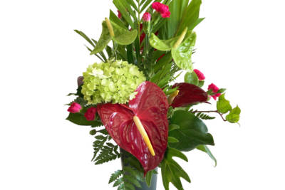 Memorial vase arrangement with a variety of maroon, red, and green flowers and foliage, in a slender dark green vase