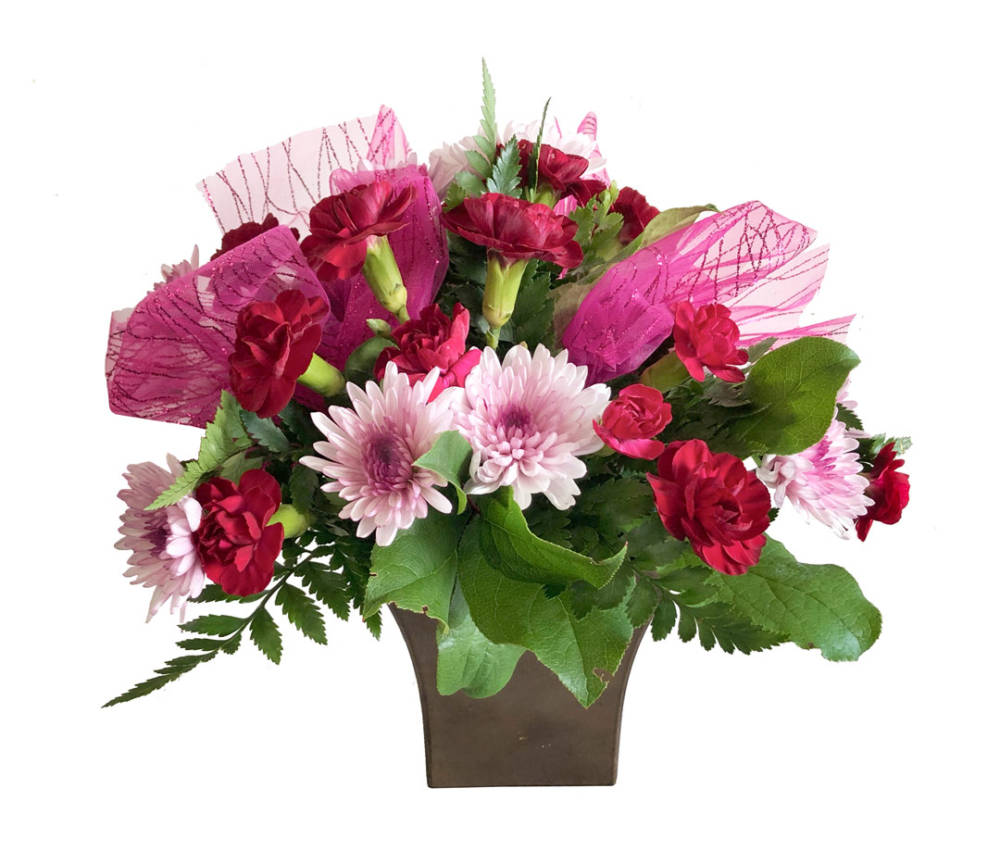 Mixed arrangement of red and pink flowers and green foliage, wrapped in pink fabric, in a dull green vase