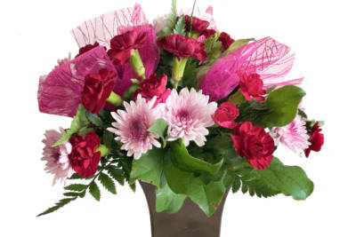 Mixed arrangement of red and pink flowers and green foliage, wrapped in pink fabric, in a dull green vase
