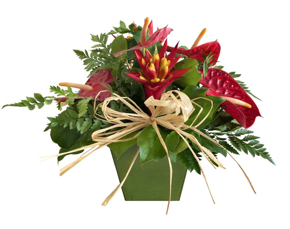 A variety of tropical, red and yellow flowers and green foliage. in a green container, with a big straw blow in the leaves